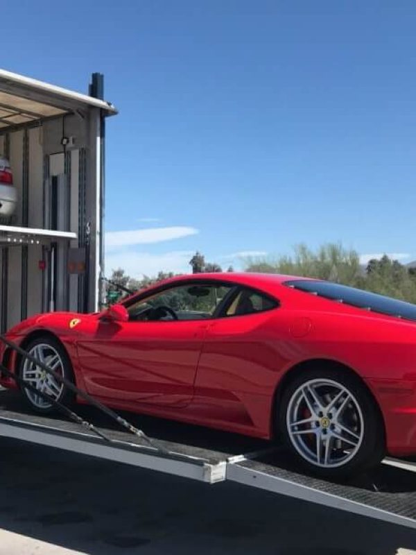 Red vehicle being loaded into an enclosed auto carrier truck